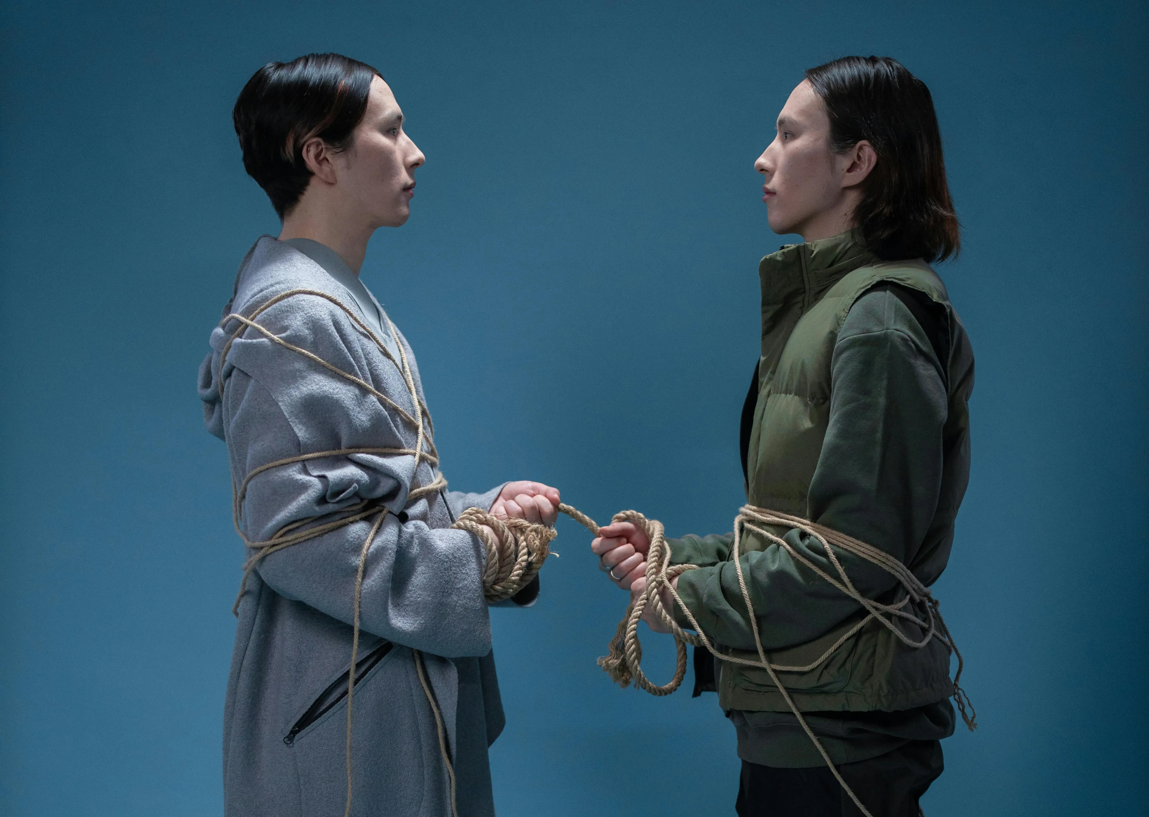 Two men staring at each other with ropes curled on their bodies connecting them