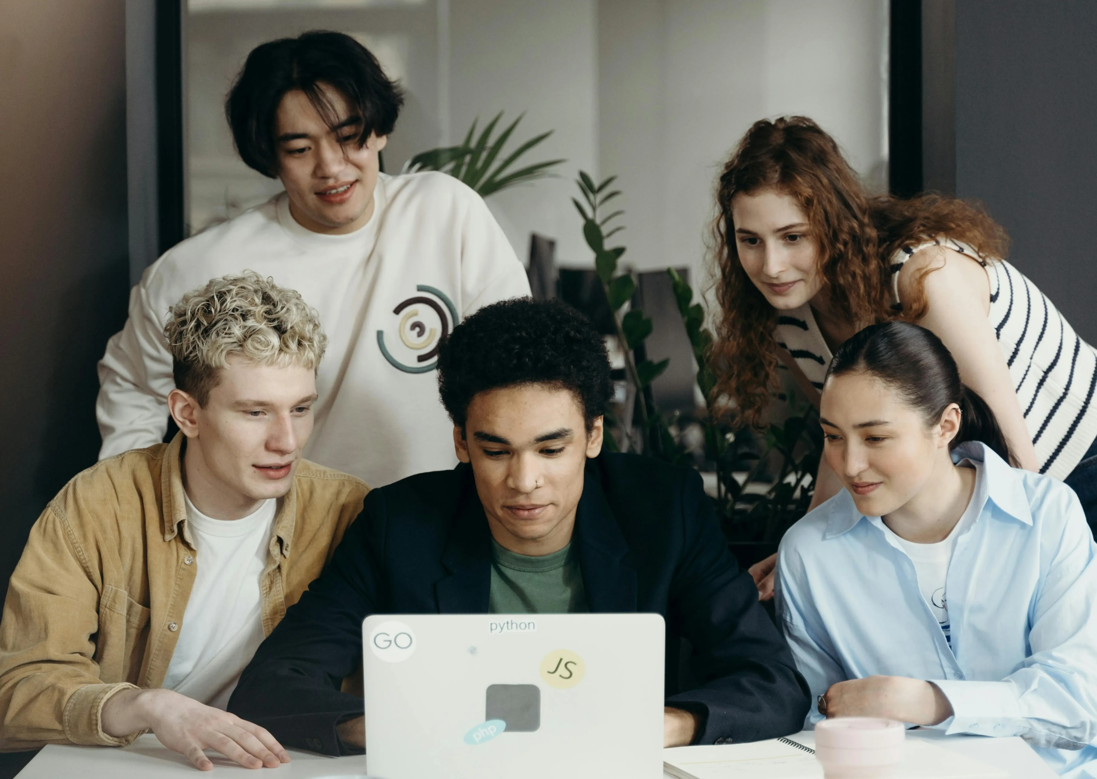 A group of young people observing their colleague working on a laptop